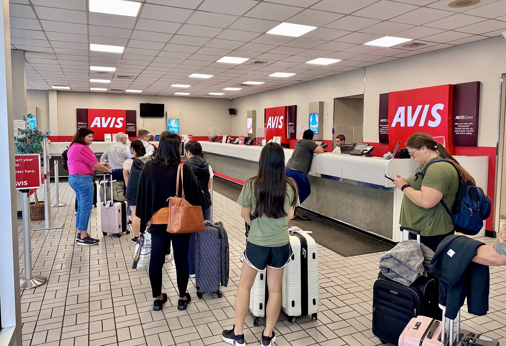 Customers wait at an Avis car rental counter, highlighting the need for vigilance against travel scams.