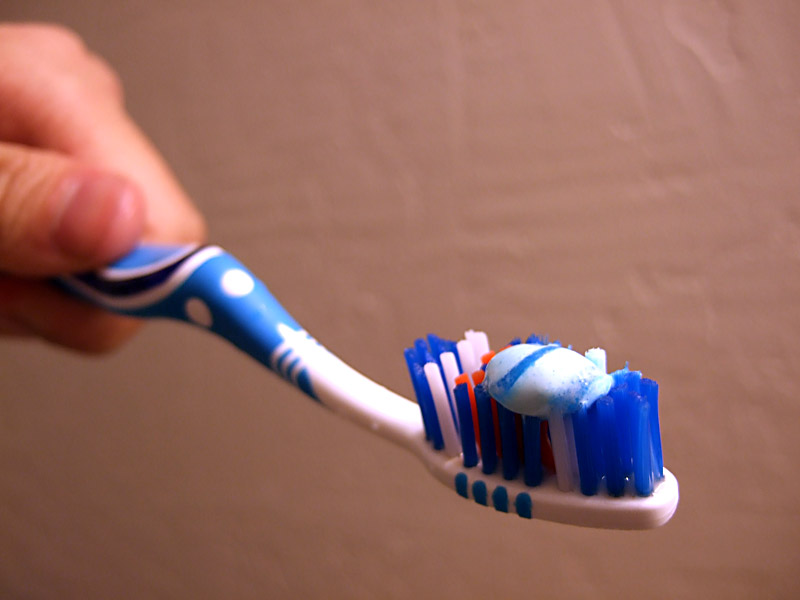 A hand applies white and blue toothpaste to a toothbrush, illustrating online safety practices.