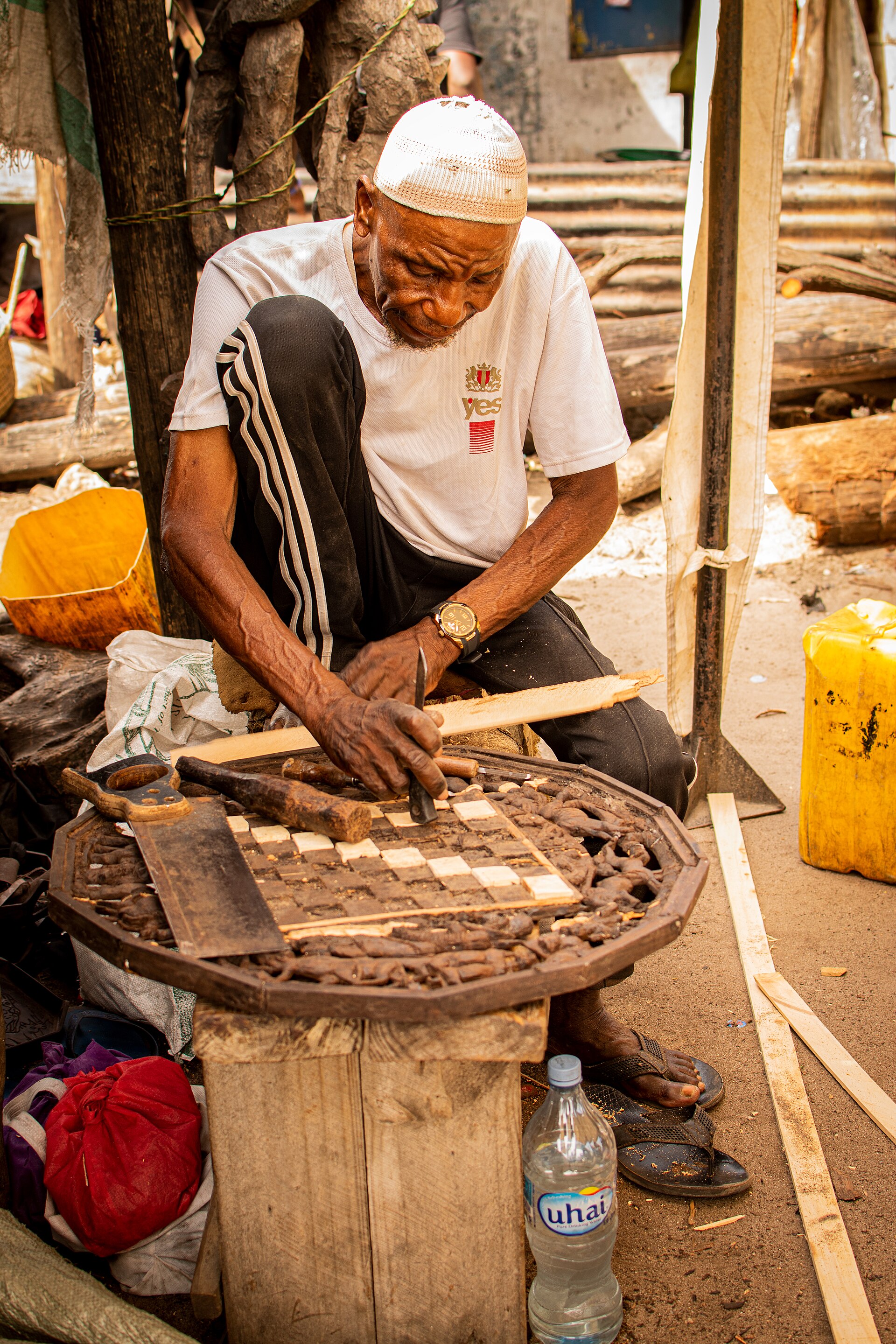 An elderly man carves wood on a Zanzibar street, highlighting the importance of online safety for all ages.